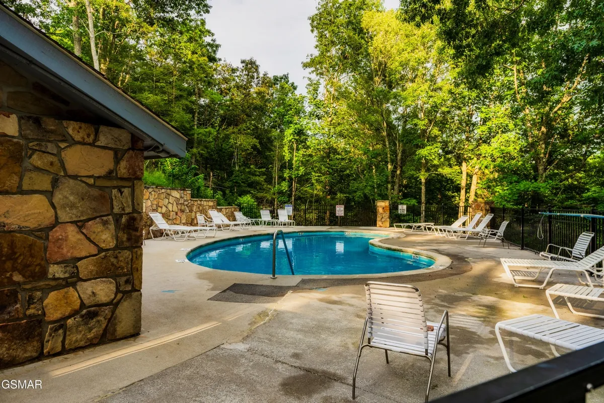 This image captures the sunlit community pool with inviting lounge chairs and a rustic stone wall, emphasizing a space perfect for swimming, sunbathing, and leisurely afternoons.