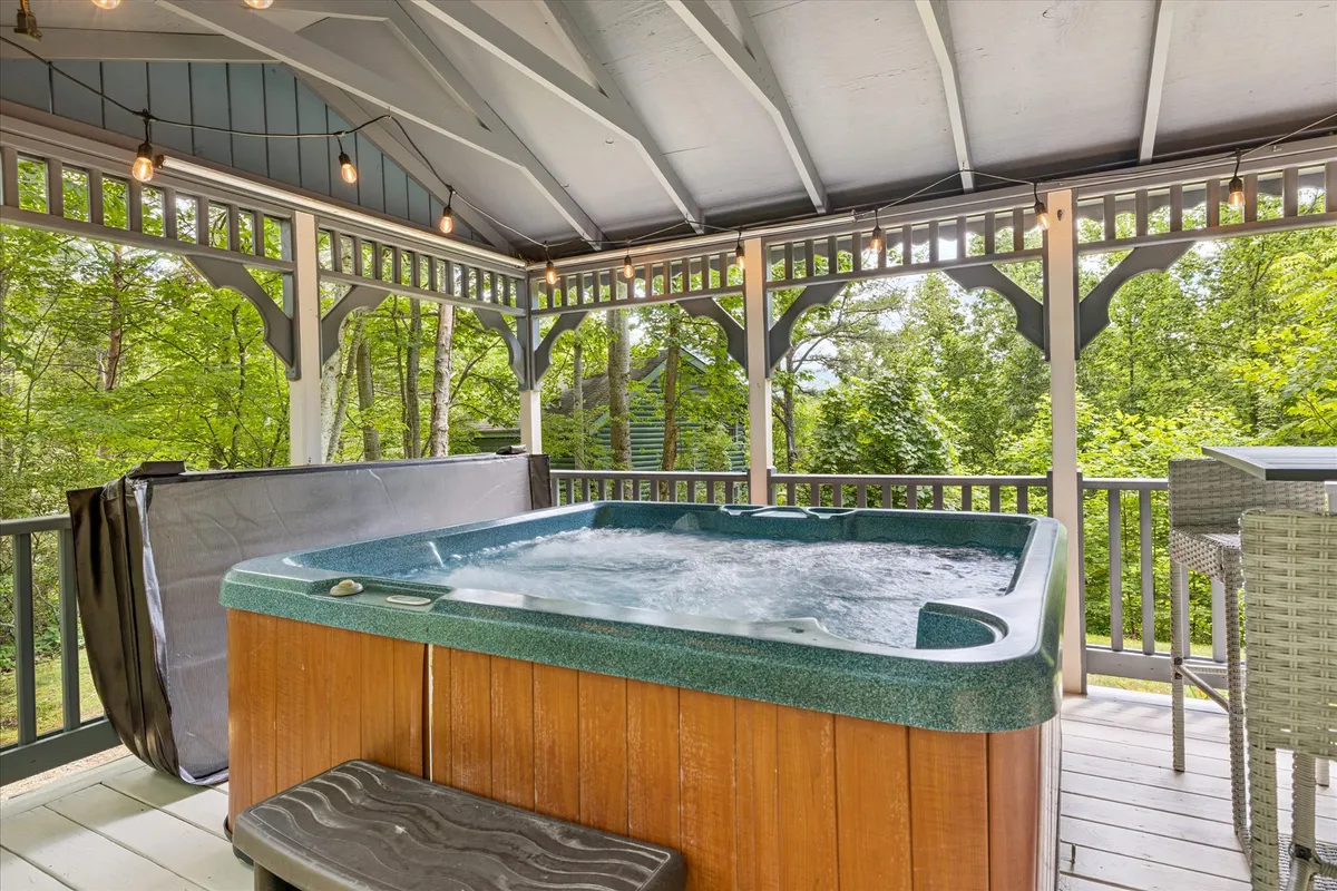 This exterior shot highlights a hot tub with wooden accents and outdoor seating, all set against a backdrop of rich greenery for a peaceful, resort-like atmosphere.