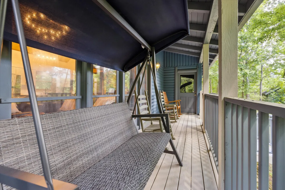 A welcoming swing bench and a pair of rocking chairs grace the porch, with a pathway leading to the door. The scene is framed by lush greenery, creating a perfect spot for couples to enjoy the fresh mountain air and quiet moments together.