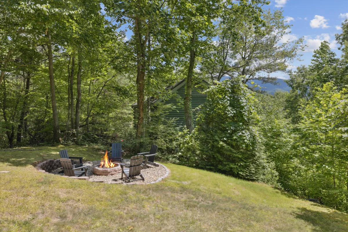 This image shows a cozy outdoor fire pit area surrounded by wooden chairs and encircled by lush trees. The setting is ideal for family gatherings, storytelling, roasting marshmallows, and stargazing, fostering a sense of togetherness and outdoor enjoyment.