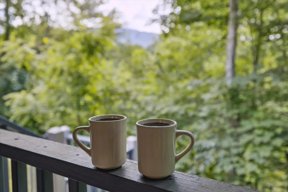 This image captures two mugs of coffee resting on a balcony railing, surrounded by lush greenery. The soft, natural light creates a serene and inviting atmosphere, perfect for intimate moments and quiet conversation. The perspective emphasizes the peaceful seclusion and natural beauty of the setting, inviting couples to imagine themselves enjoying a morning coffee together.