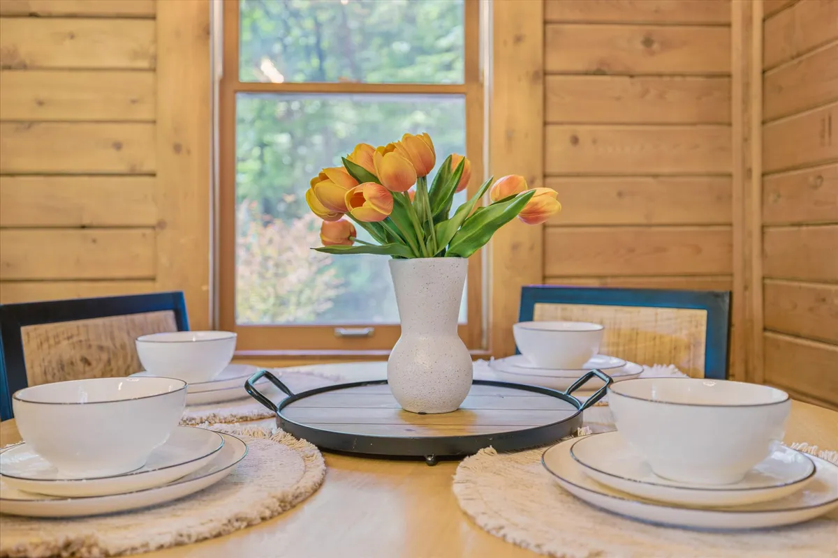 This image focuses on the dining area, featuring a beautifully set dining table, a vase of tulips, wooden walls, and comfortable chairs—setting the scene for family meals and intimate gatherings.