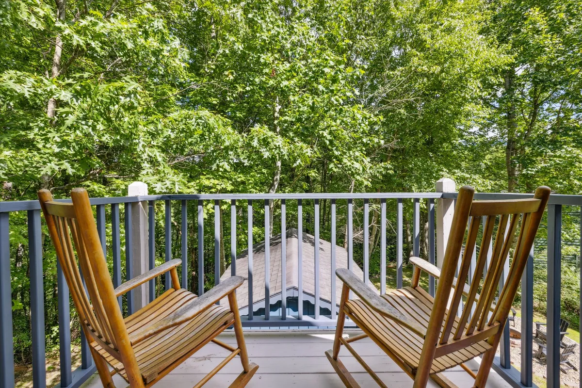 This exterior shot features a pair of classic rocking chairs on a wooden porch, surrounded by dense green foliage. The tranquil setting and inviting seating suggest a peaceful spot to unwind, perhaps watching the sunset or enjoying time together in nature.