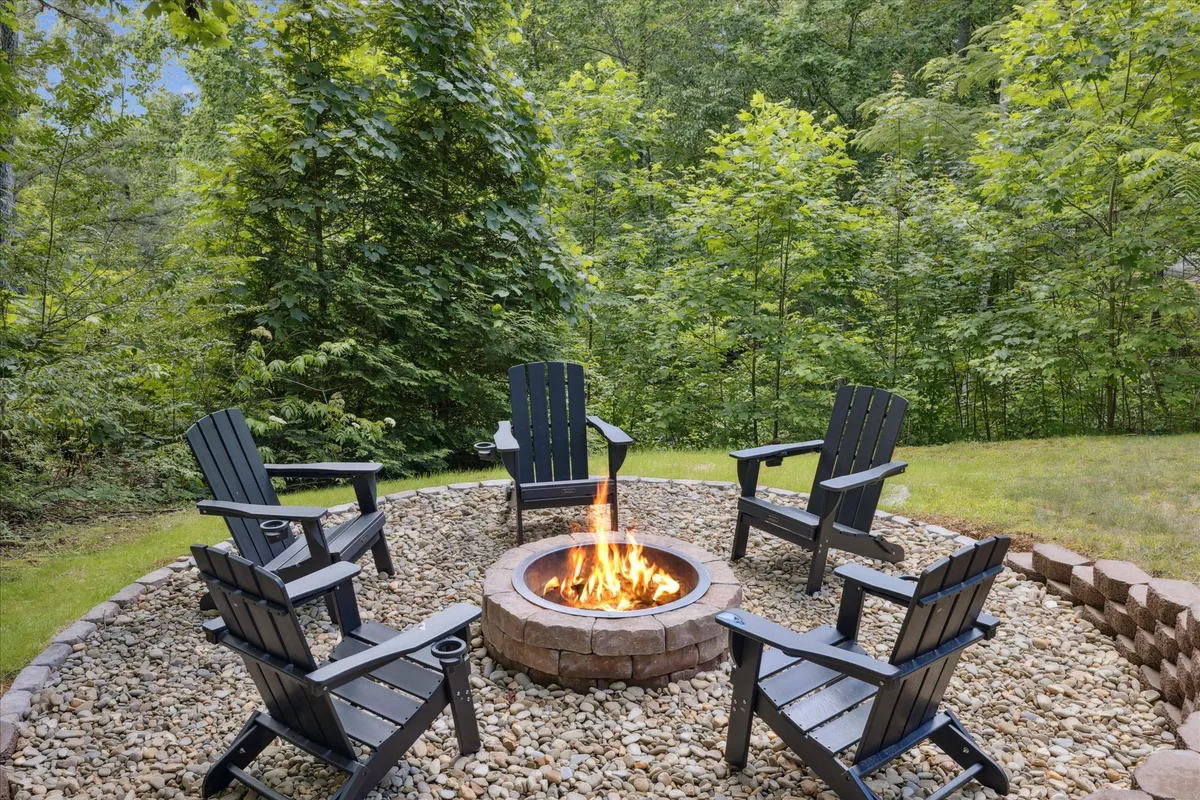 A cozy firepit ringed by Adirondack chairs, surrounded by trees and greenery. The setting is ideal for group gatherings, storytelling, and roasting marshmallows, with an inviting ambiance perfect for evening or nighttime enjoyment.
